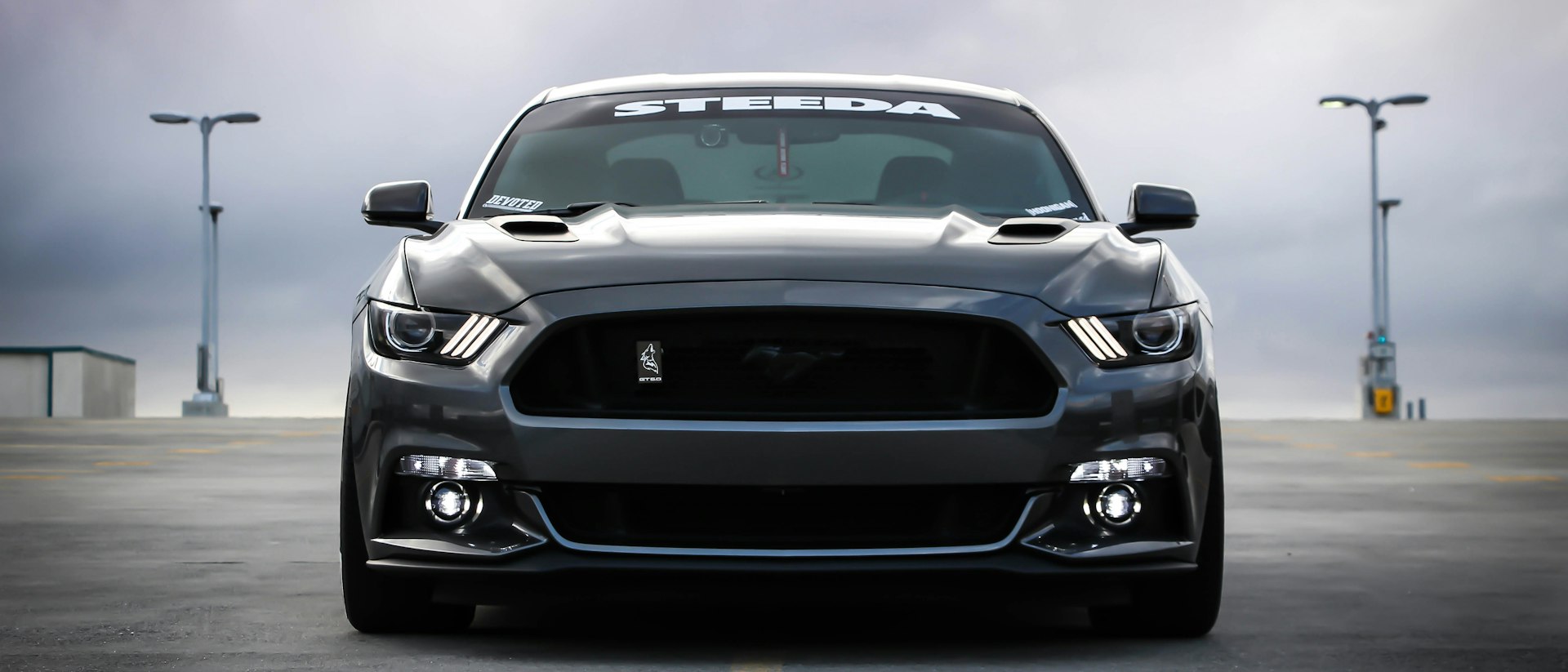 Grey muscle car photographed head-on on an empty road at dusk.