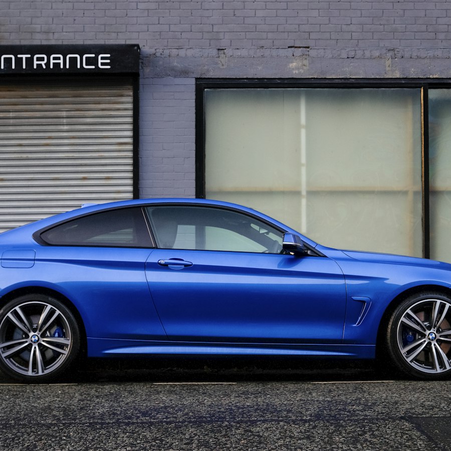 Blue coupé side profile in front of a warehouse.