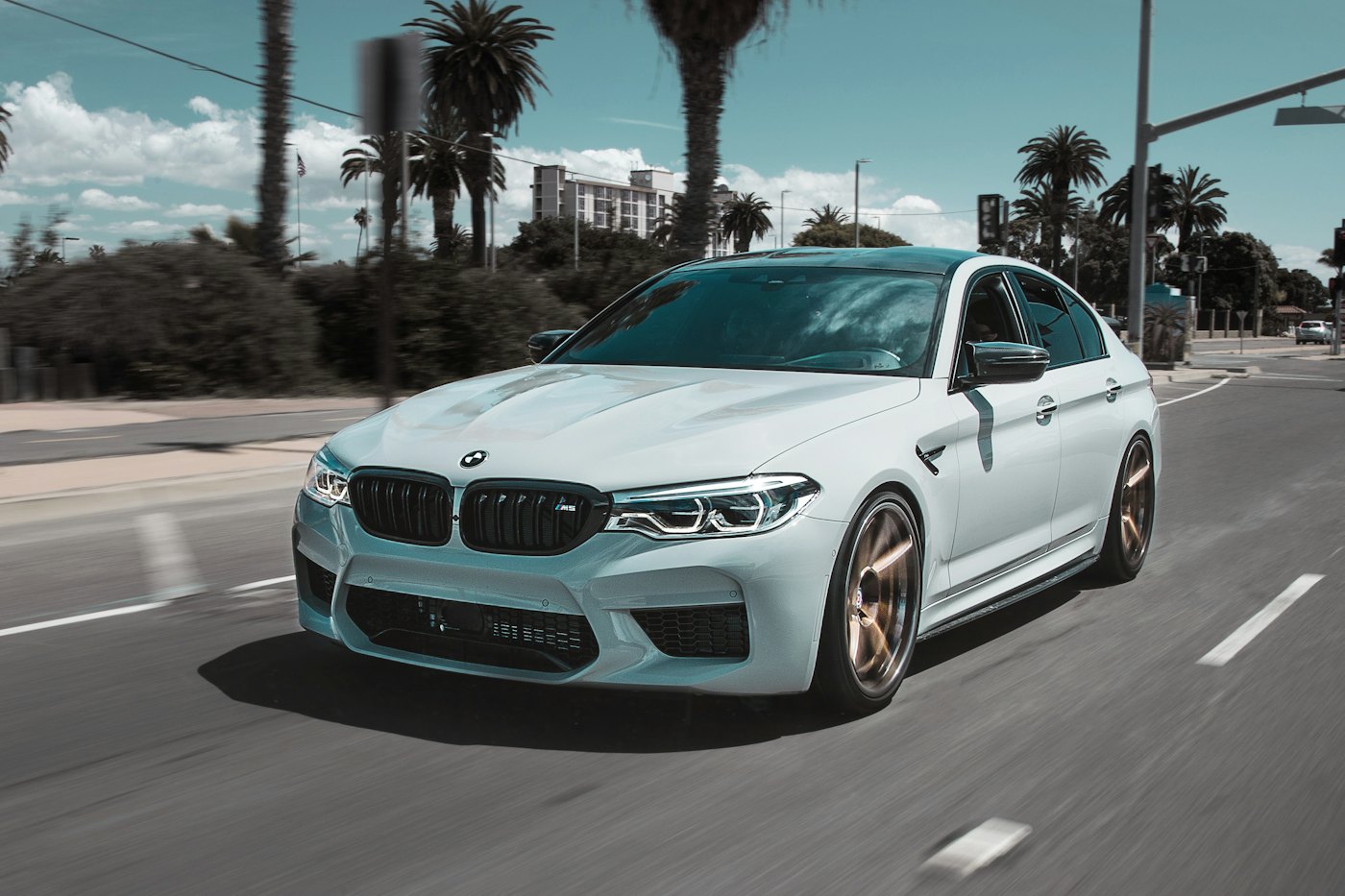 White performance saloon on a palm-lined street.