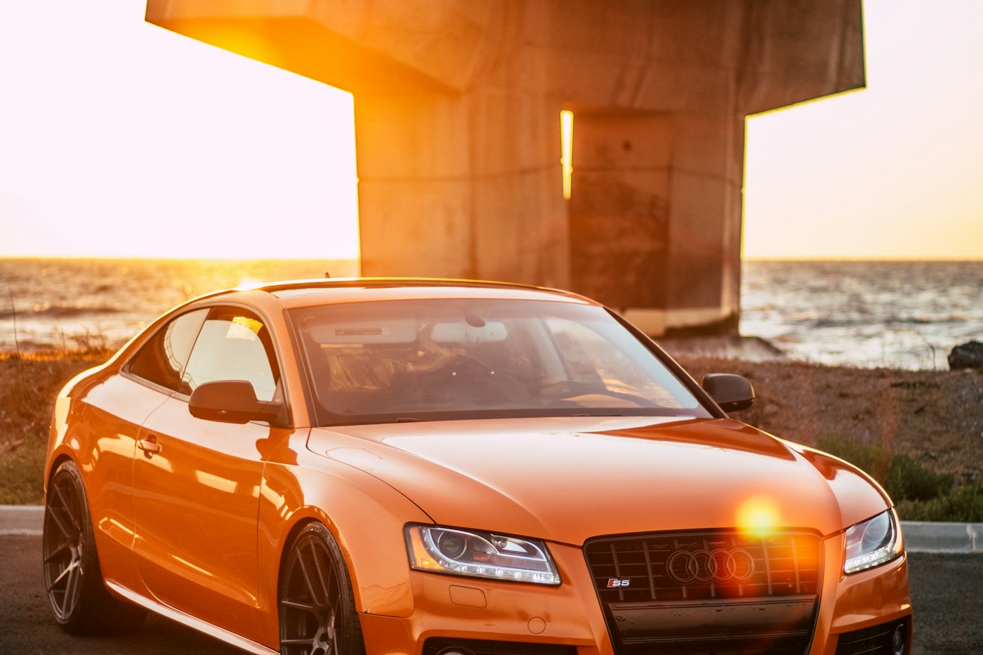 Coupé parked under a concrete structure at sunset.