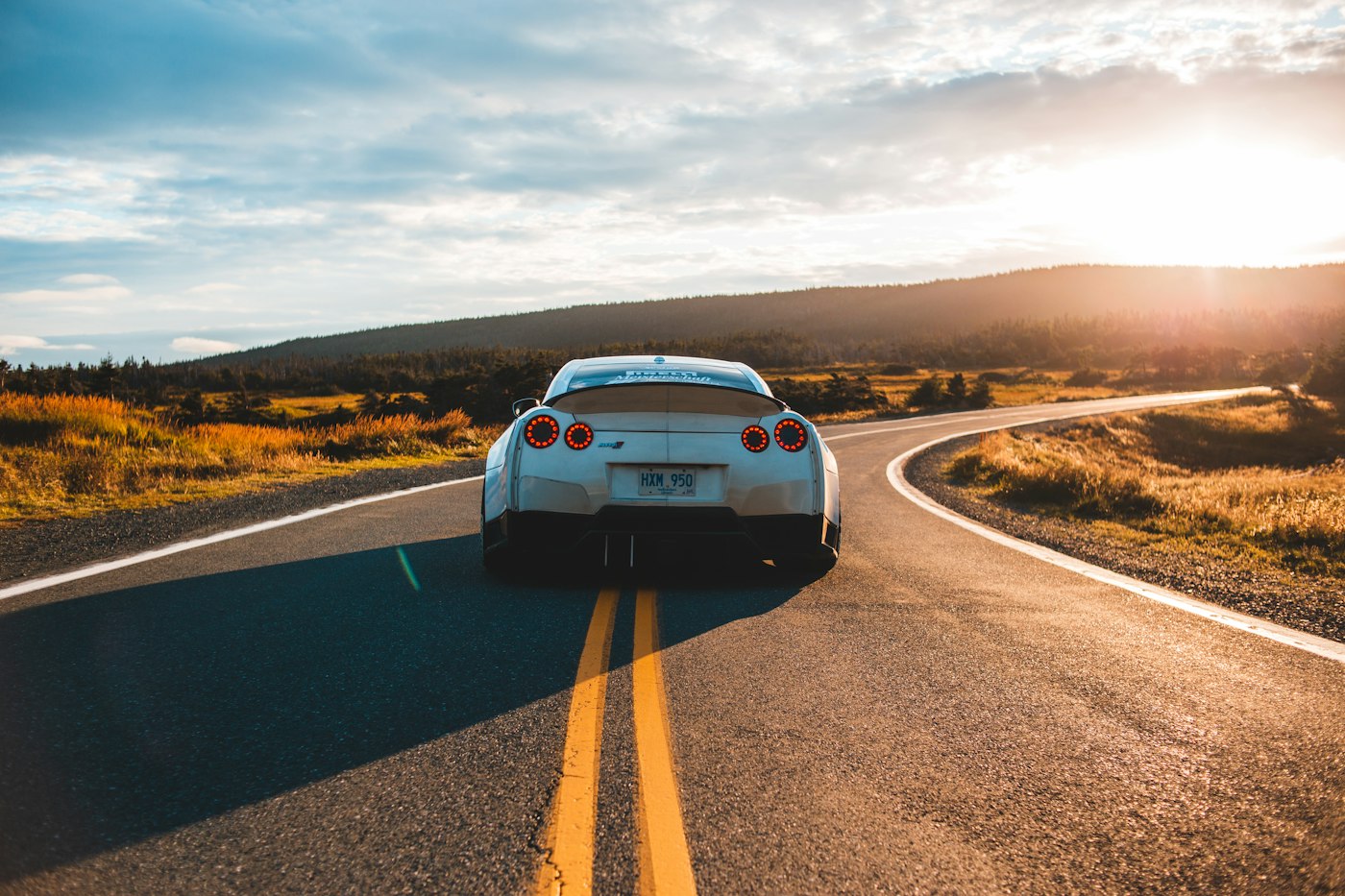 Sports car driving away down a winding road at sunset.
