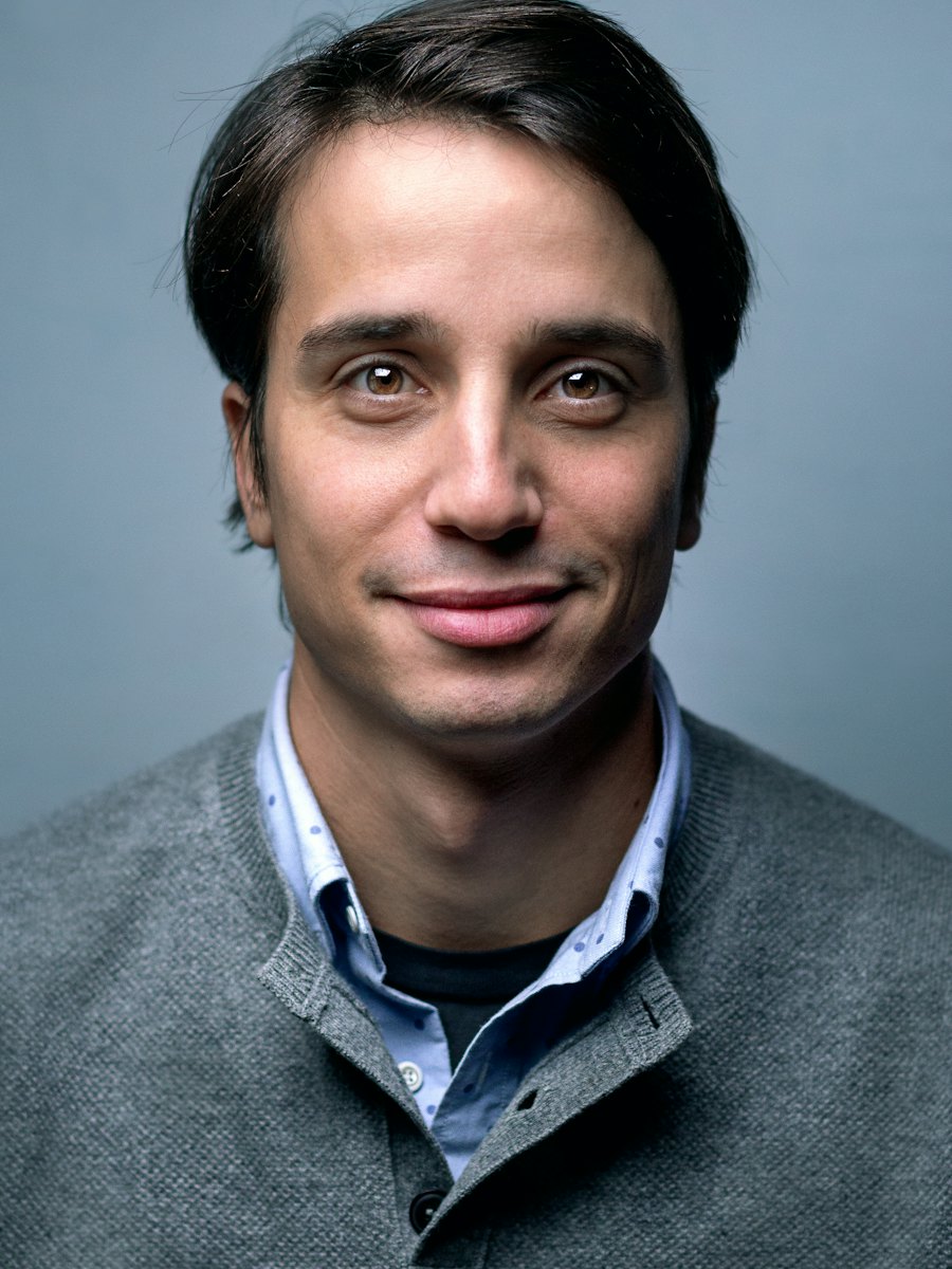 Studio headshot of a smiling man against a grey backdrop.
