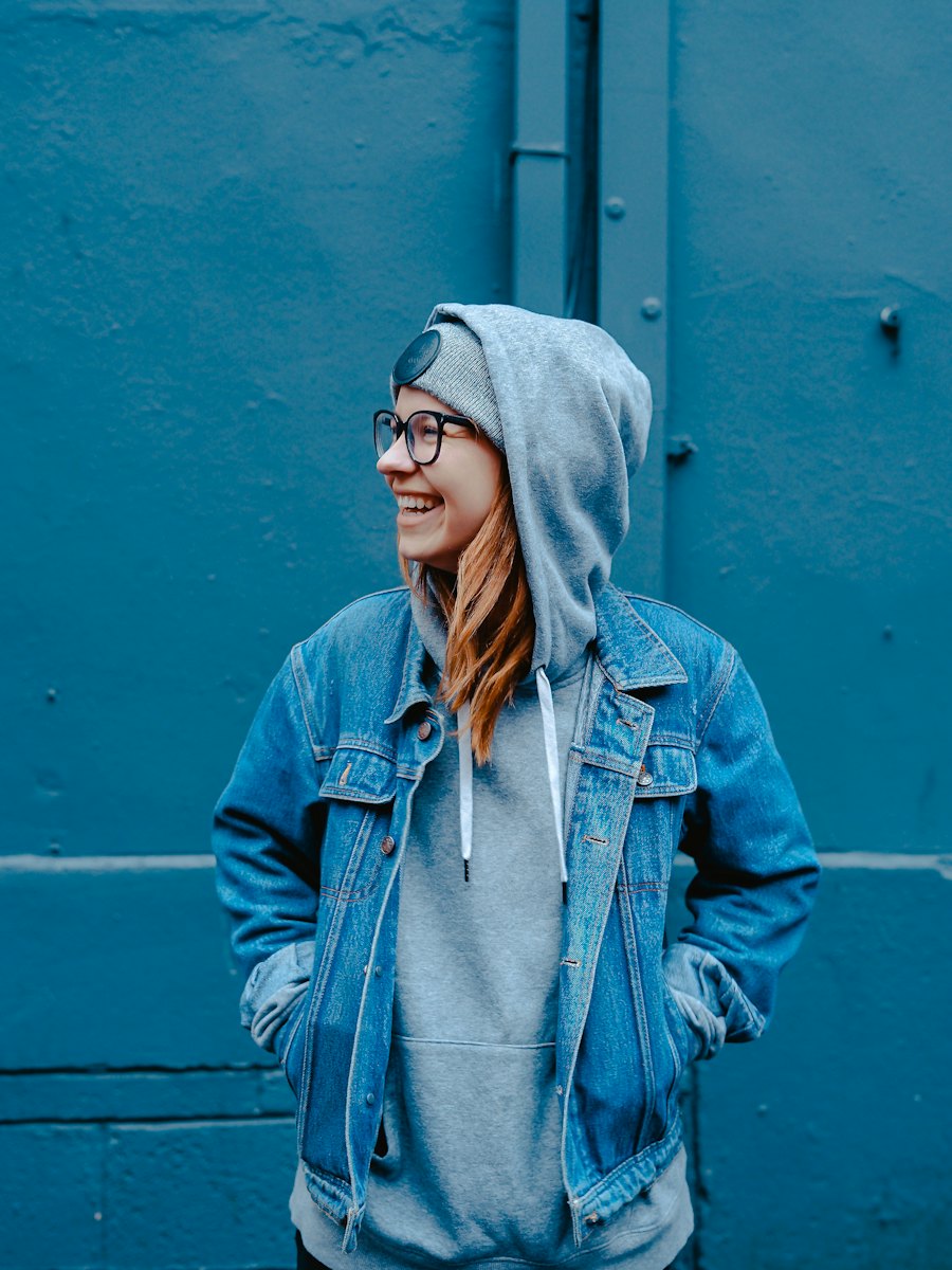 Portrait of a woman in a denim jacket against a blue wall.